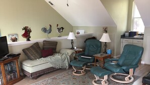 Een gezellige woonkamer met een bank, twee groene fauteuils, een salontafel, een televisie en een boekenkast.