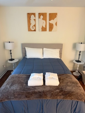 A bed with a blue bedspread, two white pillows, and a brown throw blanket. There are two wall-mounted artworks depicting abstract figures. - Golf View Condo - Pool Steps Away -  Beach Access (Hilton Head Island)