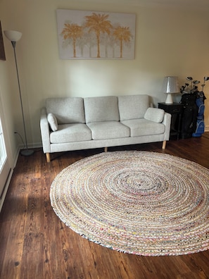A living room with a grey sofa, a colorful circular rug, a lamp, and a golf bag. - Golf View Condo - Pool Steps Away -  Beach Access (Hilton Head Island)