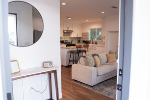 A modern kitchen with white cabinets, a round mirror, and a dining area with a sofa and chairs. - 4BR Home w EV Charger, Outdoor 75" TV & Backyard Oasis Near Disney, SoFi & more (Pico Rivera)