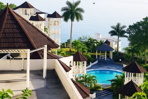 Um resort com piscina, palmeiras e vista para o mar.