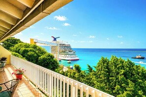 Ein Balkon mit Blick auf ein Kreuzfahrtschiff, üppigem Grün und einem strahlend blauen Himmel.