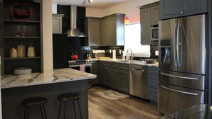 Una cocina moderna con armarios oscuros, electrodomésticos de acero inoxidable, encimera de mármol y suelo de madera.