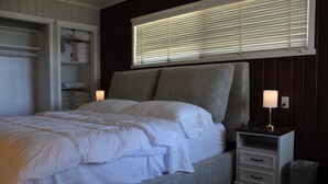 Un dormitorio con cama, mesita de noche, lámpara, ventana con persianas y armario.