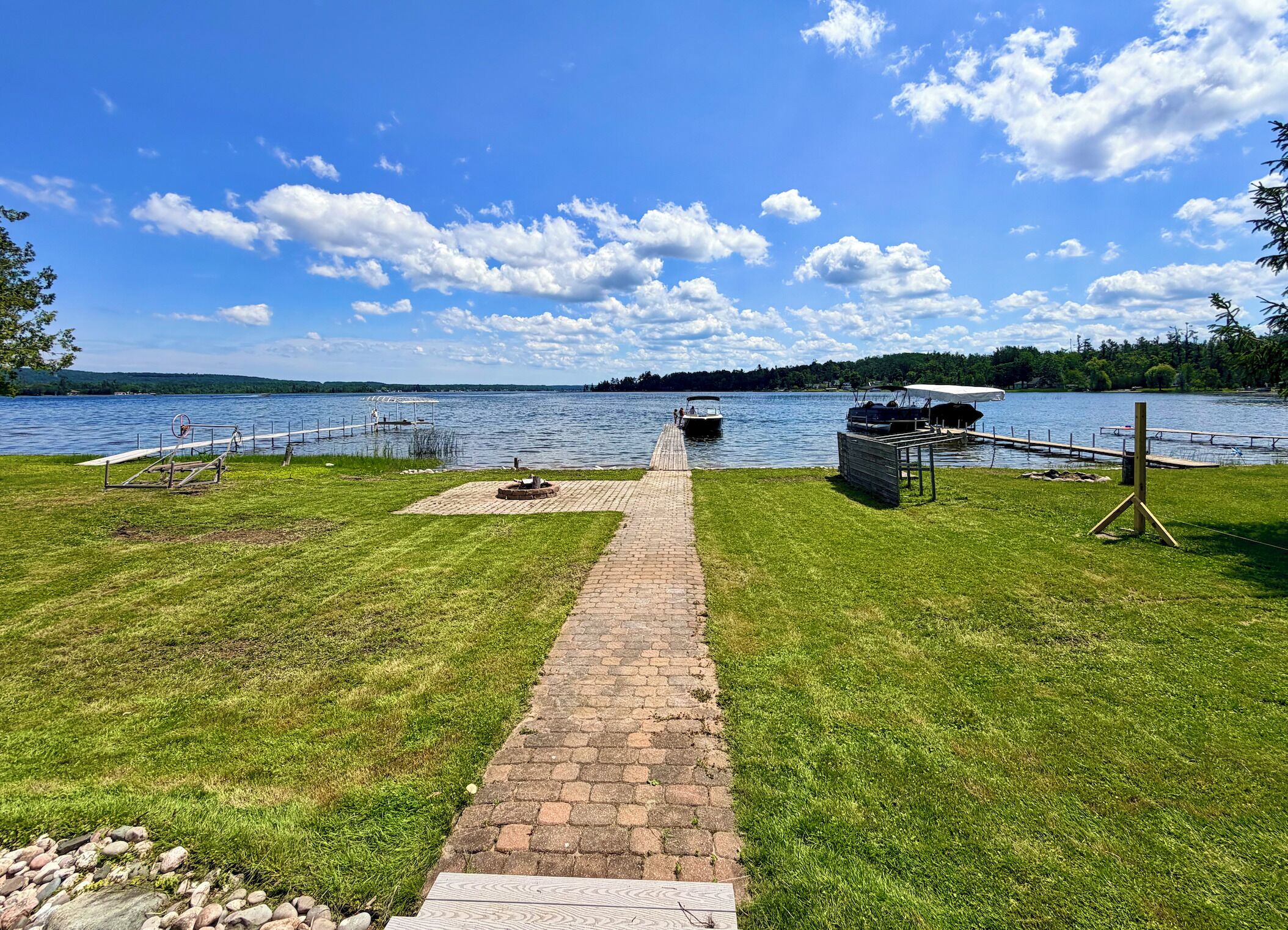 A lakeside walkway leading to a dock with a boat, surrounded by grassy areas and trees.