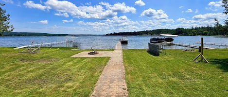 A lakeside walkway leading to a dock with a boat, surrounded by grassy areas and trees.