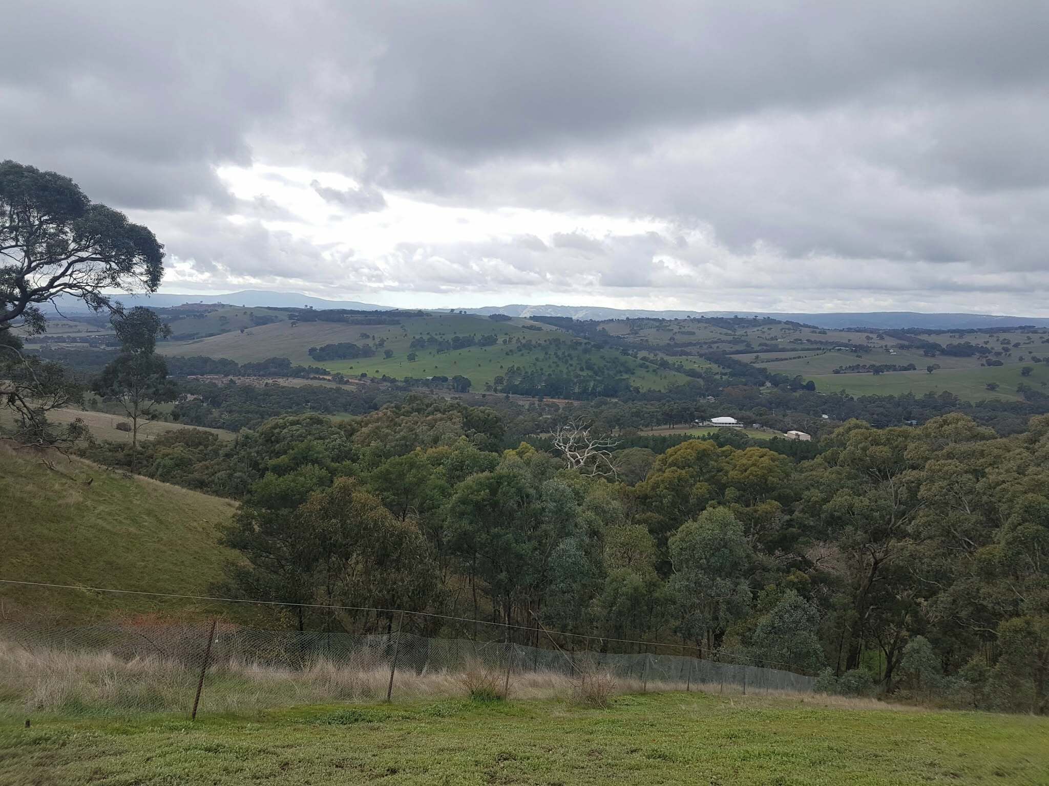 A rural landscape with rolling hills, a fence, and a distant building.