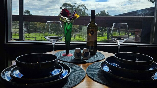 A dining table with two plates, a bottle, and a vase with flowers. - Apple Tree Studio - country luxury self-contained studio (Kilmore)