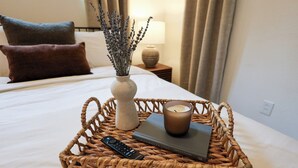 Un lit bien fait, avec une télécommande, un livre et une bougie dans un panier en osier.
