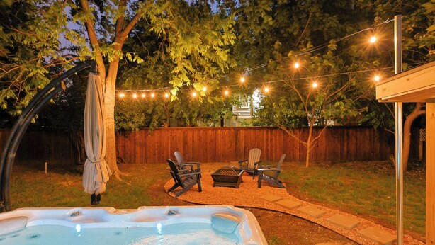Un jardin avec un jacuzzi, un espace salon extérieur, des guirlandes lumineuses et une clôture en bois.