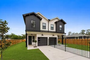 A two-story house with a front garage, a small front yard, and a wooden fence. - Maison Covington: Modern Luxury 3BR Retreat Near Houston Hotspots (Houston)
