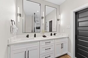 A bathroom with two mirrors, a white vanity, and a dark door. - Maison Covington: Modern Luxury 3BR Retreat Near Houston Hotspots (Houston)