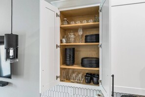 A kitchen cabinet with shelves containing glassware and black plates. - Maison Covington: Modern Luxury 3BR Retreat Near Houston Hotspots (Houston)