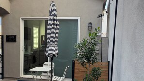 En terrasse med et bord og stole, en stribet parasol, en potteplante og en bygning med en garageport.