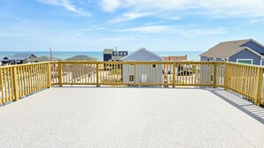 A beachside property with a fenced deck, a gravel patio, and houses in the background. - Cozy 1 bedroom house in serene Kitty Hawk with Rooftop views of Ocean and sunset (Kitty Hawk)