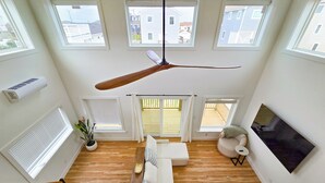 A spacious loft with a ceiling fan, large windows, a TV, and a staircase. - Cozy 1 bedroom house in serene Kitty Hawk with Rooftop views of Ocean and sunset (Kitty Hawk)