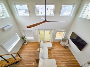 A spacious loft with a ceiling fan, large windows, a TV, and a staircase.