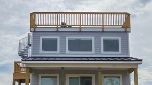 A two-story building with a balcony, a staircase, and a porch. - Cozy 1 bedroom house in serene Kitty Hawk with Rooftop views of Ocean and sunset (Kitty Hawk)
