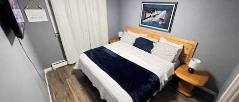 Une chambre à coucher comprenant un lit, des tables de chevet, une commode, un tableau accroché au mur et une fenêtre avec des rideaux.