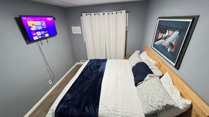 Una camera d'albergo con un letto, una TV fissata al muro, una finestra con tende e un quadro incorniciato.