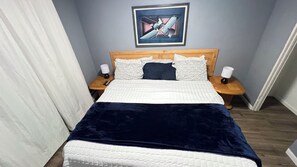 Un letto con copriletto bianco e blu scuro, due lampade ai lati, una testiera in legno e un quadro astratto appeso alla parete.