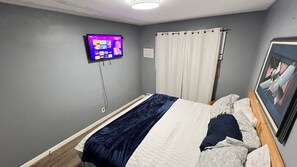 Una camera da letto con un letto, una televisione a muro, una finestra con tende e un quadro incorniciato.