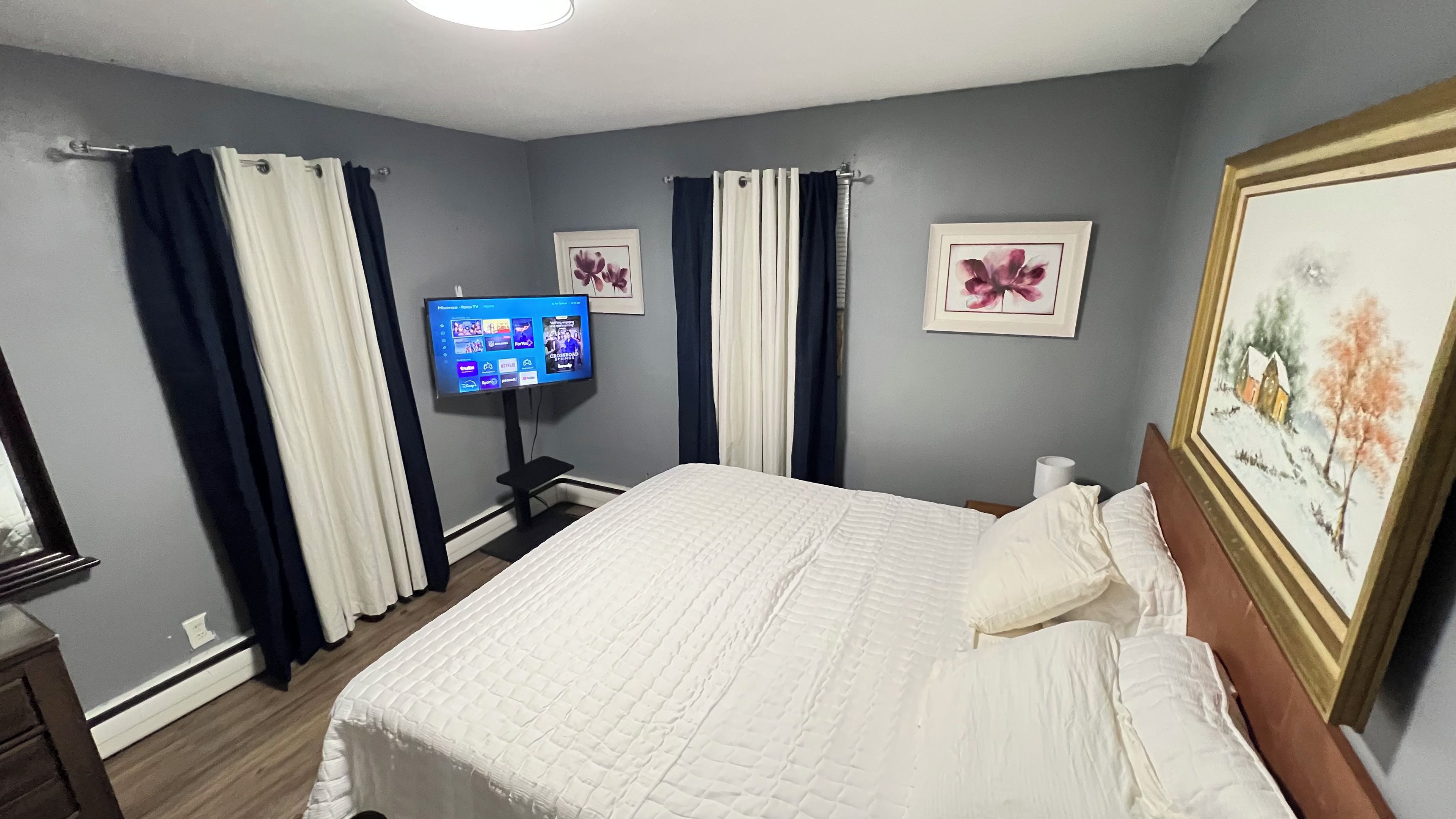 Ein Hotelzimmer mit einem Bett, Vorhängen, einem Flachbildfernseher und gerahmten Kunstwerken.