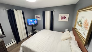 Una camera d'albergo con un letto, tende, una TV a schermo piatto e opere d'arte incorniciate.