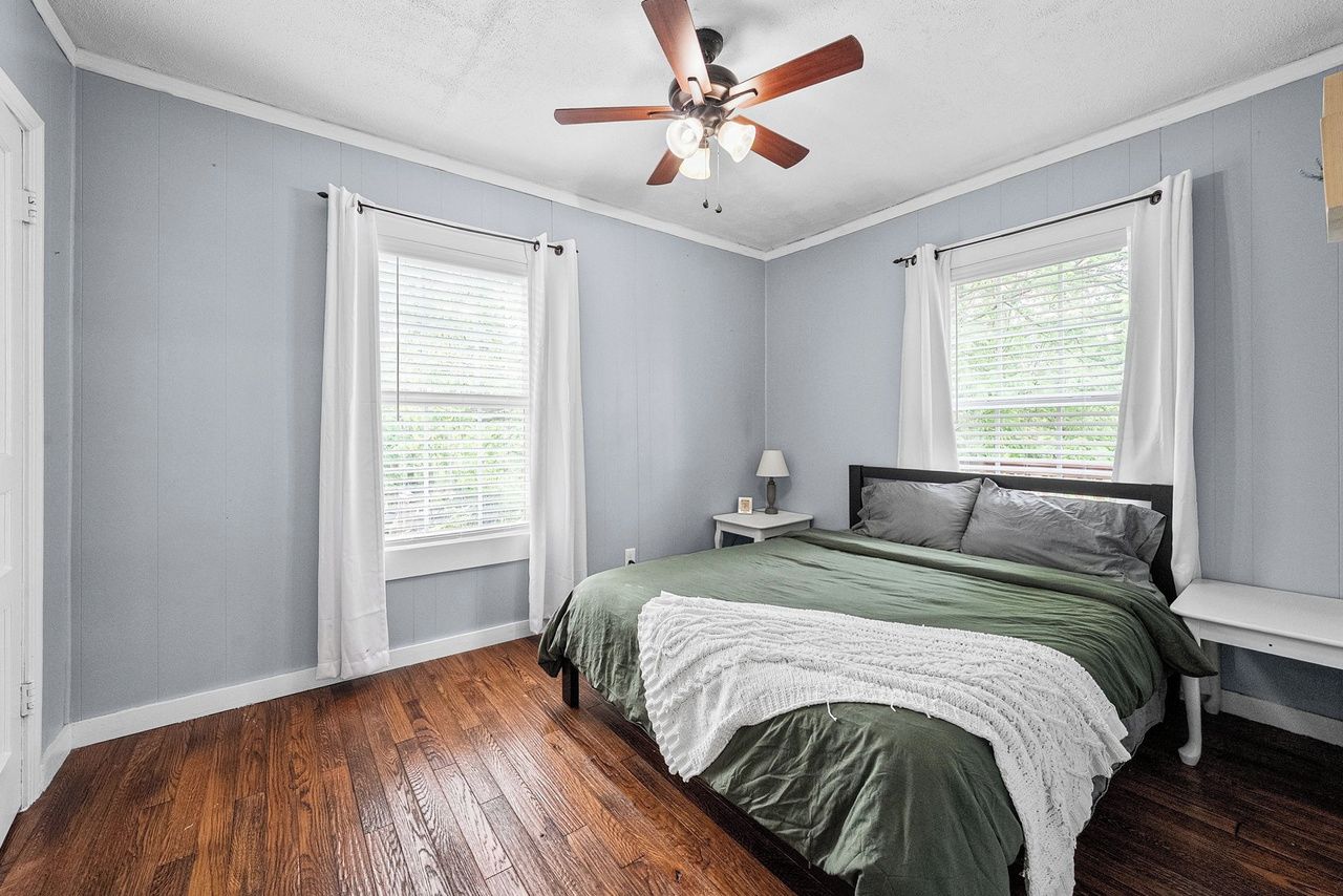 A bedroom with a bed, a ceiling fan, and two windows with curtains.