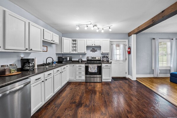 A modern kitchen with white cabinetry, stainless steel appliances, and a wooden floor.
