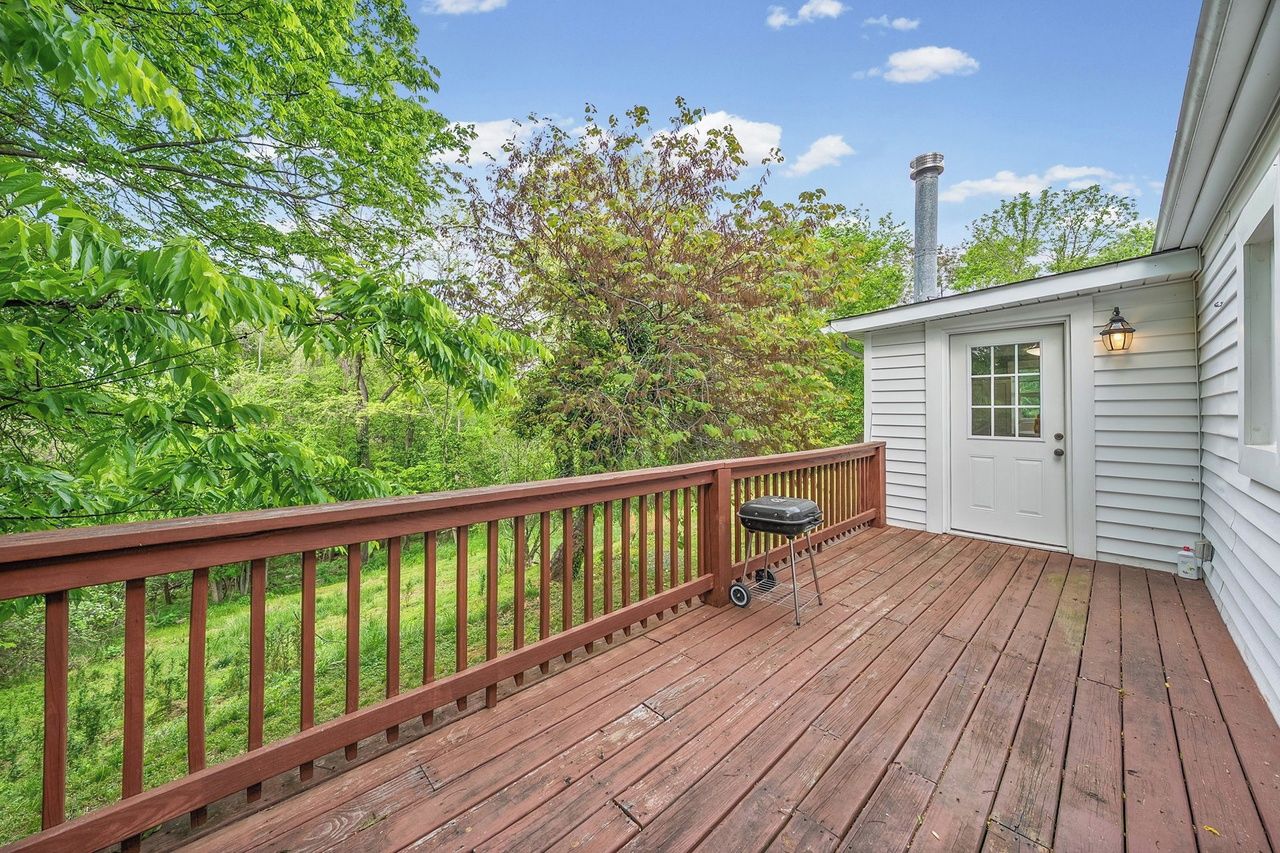 A wooden deck with a barbecue grill, a white door, and a chimney.