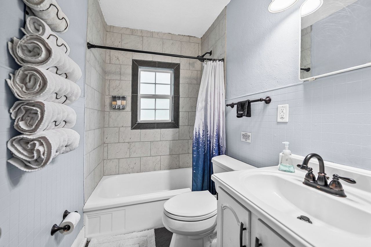A bathroom with a bathtub, toilet, and sink. There are towels on the wall, a window, and a shower curtain.