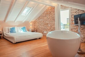 A bedroom with a large bed, a stone wall, a skylight, and a bathtub. - Villa Nerea, Private Villa Near Taormina (Taormina)