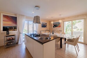 A modern kitchen with a central island, stainless steel appliances, and a dining area with a table and chairs. - Villa Nerea, Private Villa Near Taormina (Taormina)