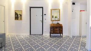 Ein Flur mit gemusterten Bodenfliesen, einer weißen Tür, einem Holzschrank mit Spiegel und einem gerahmten Bild an der Wand.
