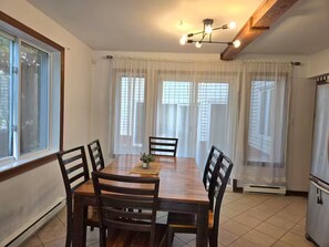 A dining area with a wooden table, six chairs, a small plant, and a modern chandelier. - 6BedR with 7 beds Single house 3 private parking (Brossard)