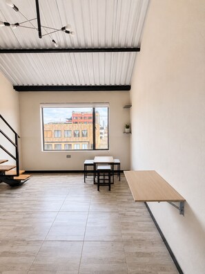 A spacious room with a large window, a wooden table, a bench, and a staircase. - Central lodging (Bogotá)