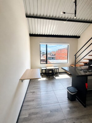 A modern kitchen with a gas stove, a dining area with a bench and stools, and a large window offering a view of buildings. - Central lodging (Bogotá)