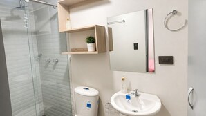 Et moderne badeværelse med toilet, håndvask, brusebad og et spejl.