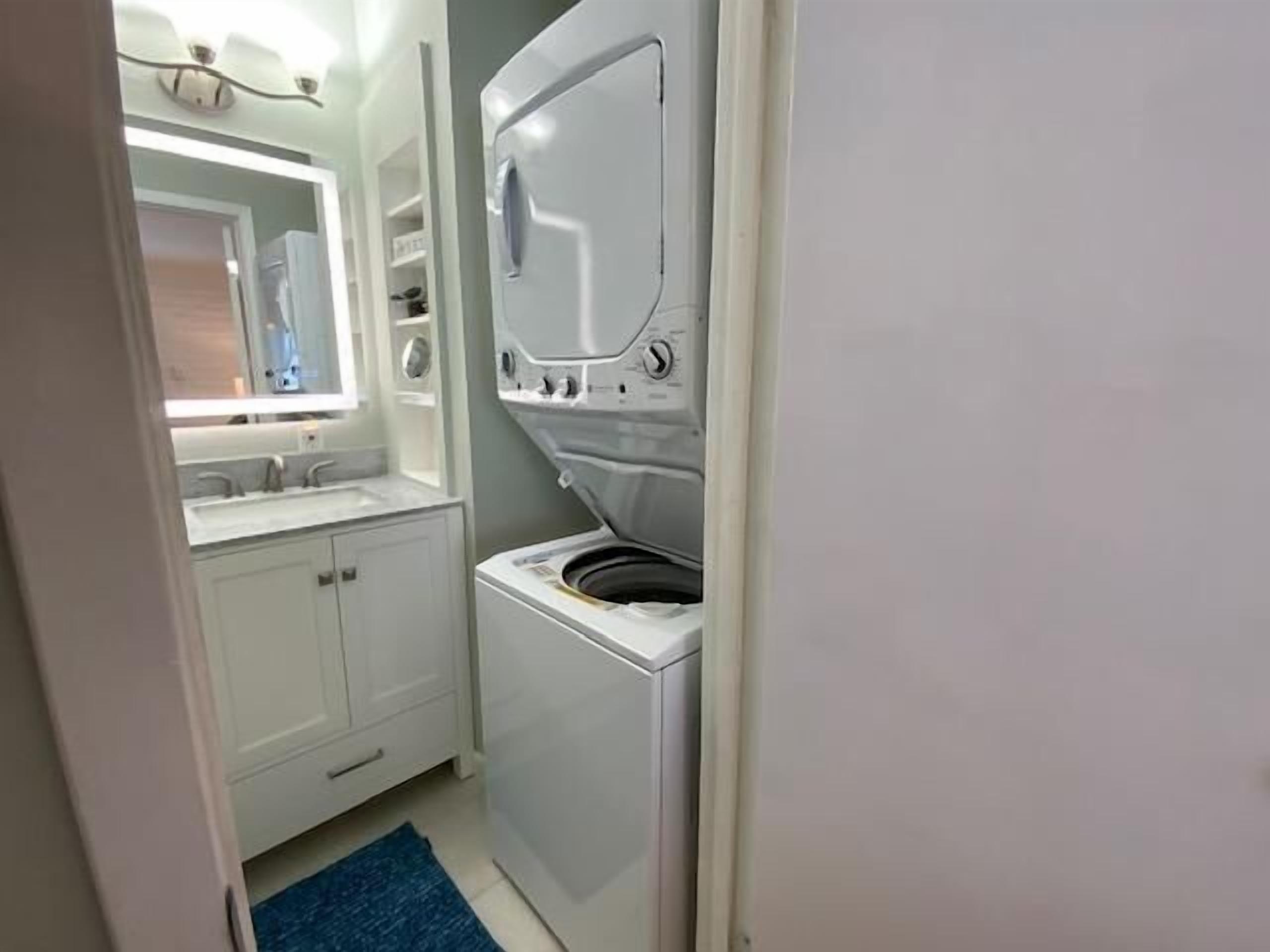 A compact bathroom with a built-in washing machine, a sink, and a mirror.