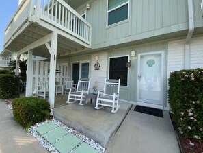 A two-story building with a porch, white railings, and a small garden area. - EC122 Shared Pool, Pet Friendly, Boardwalk to the Beach (Port Aransas)