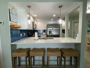 A modern kitchen with a central island, stainless steel appliances, and a blue backsplash. - EC122 Shared Pool, Pet Friendly, Boardwalk to the Beach (Port Aransas)