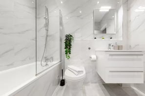 A modern bathroom with a glass-enclosed shower, a toilet, a sink with a mirror, and a plant.