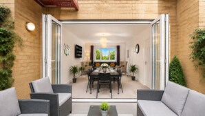 Un patio moderno con mobiliario de mimbre, una mesa de comedor para cuatro personas y plantas en macetas.