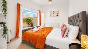 Un dormitorio con cama, radiador, ventana con cortinas, una planta y una obra de arte colgada en la pared.