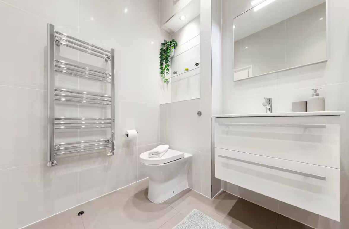 A modern bathroom with a glass shower enclosure, a toilet, a sink with a mirror, and a plant on the wall.
