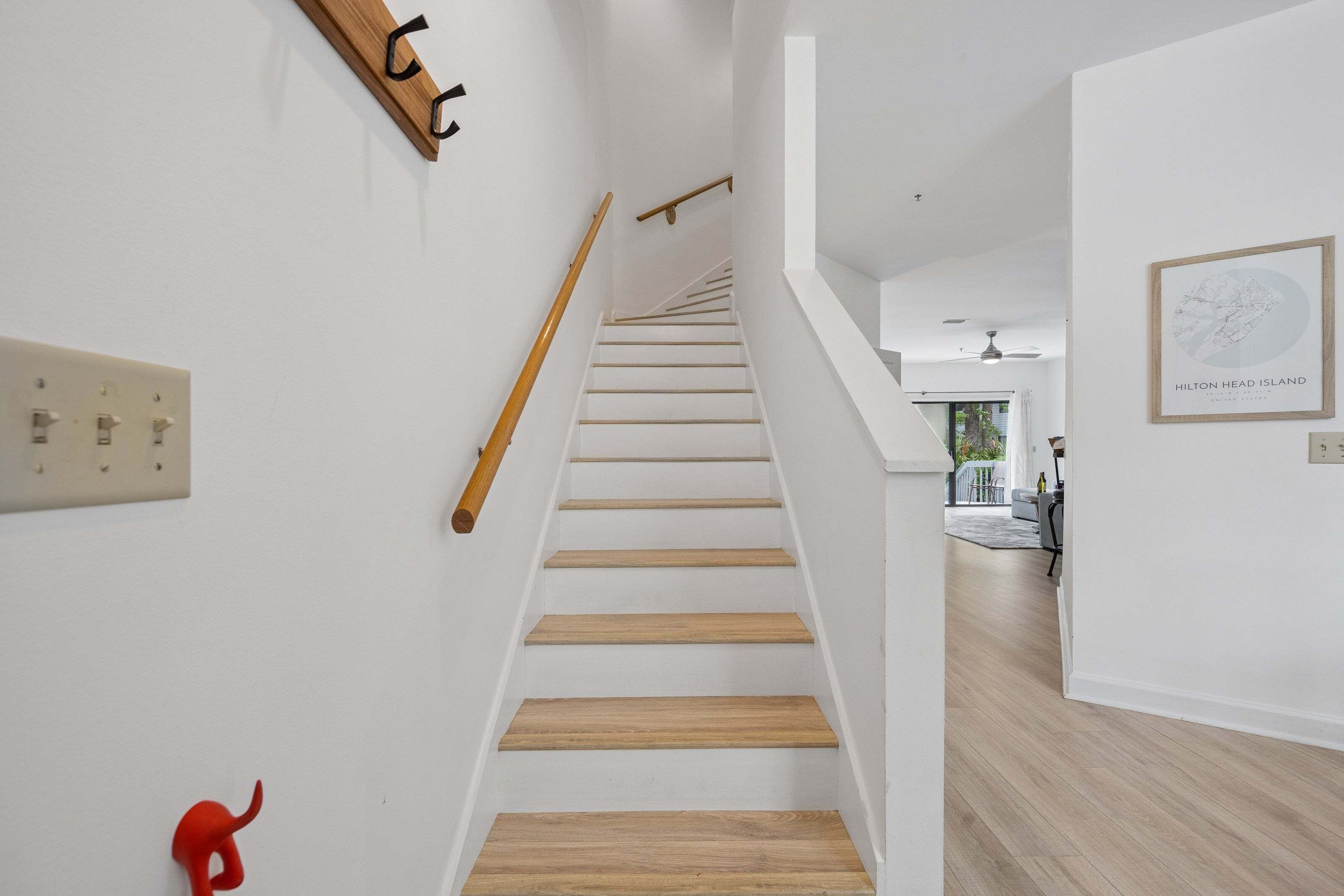 Una escalera de madera con barandilla que lleva a una habitación con pared blanca y un mapa enmarcado.
