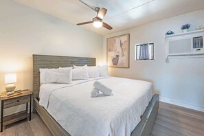 Un dormitorio con cama, mesita de noche, ventilador de techo, ventana con cortinas y aire acondicionado instalado en la pared.