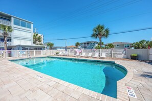 A swimming pool with lounge chairs, a lifeguard stand, and a white fence.