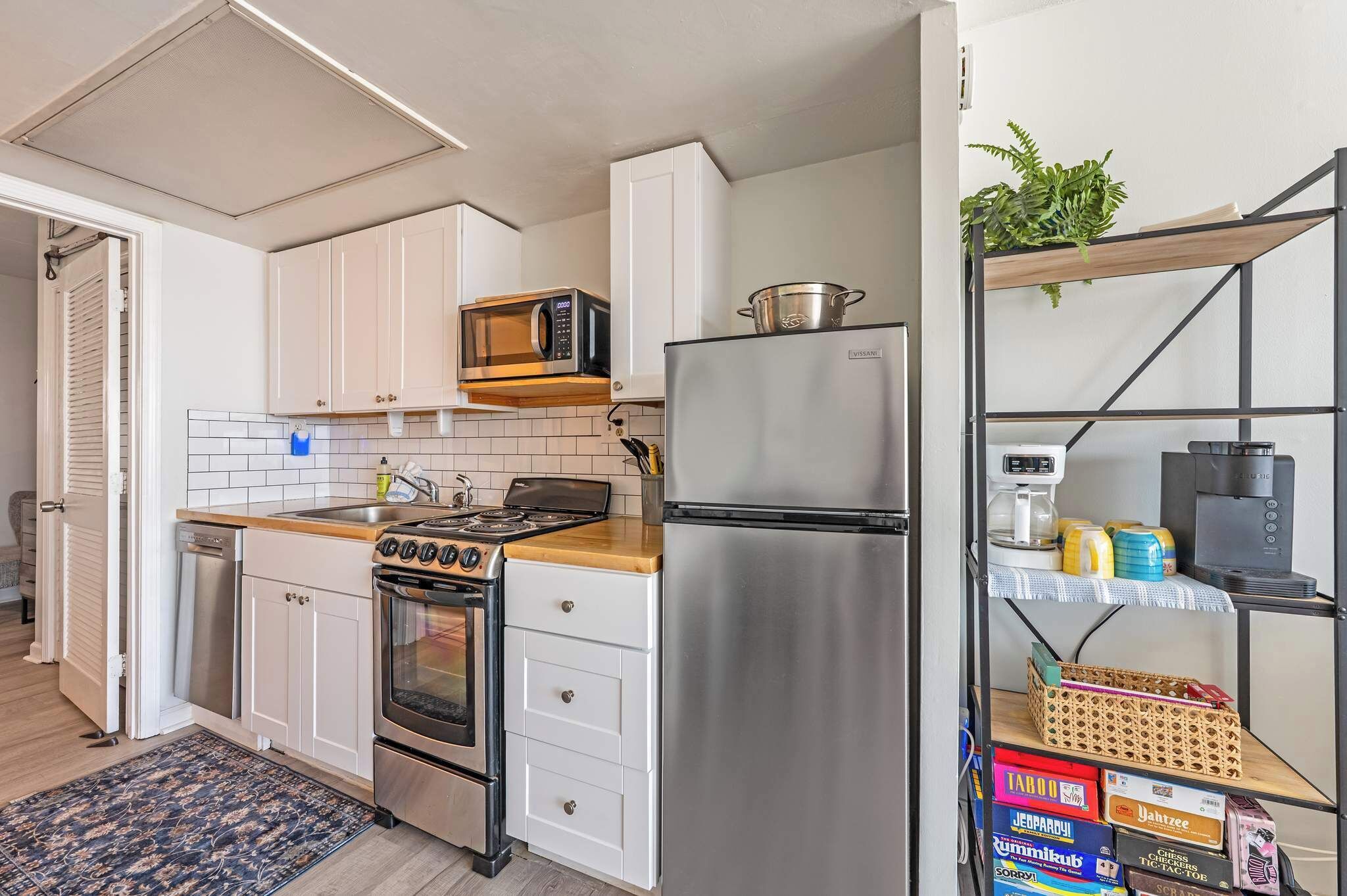 A compact kitchen with a microwave, stove, refrigerator, and a shelf with various items.